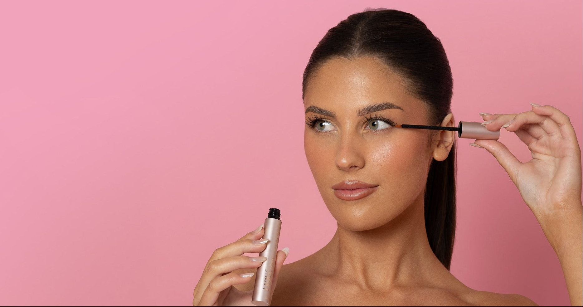 Woman applying mascara against a pink background