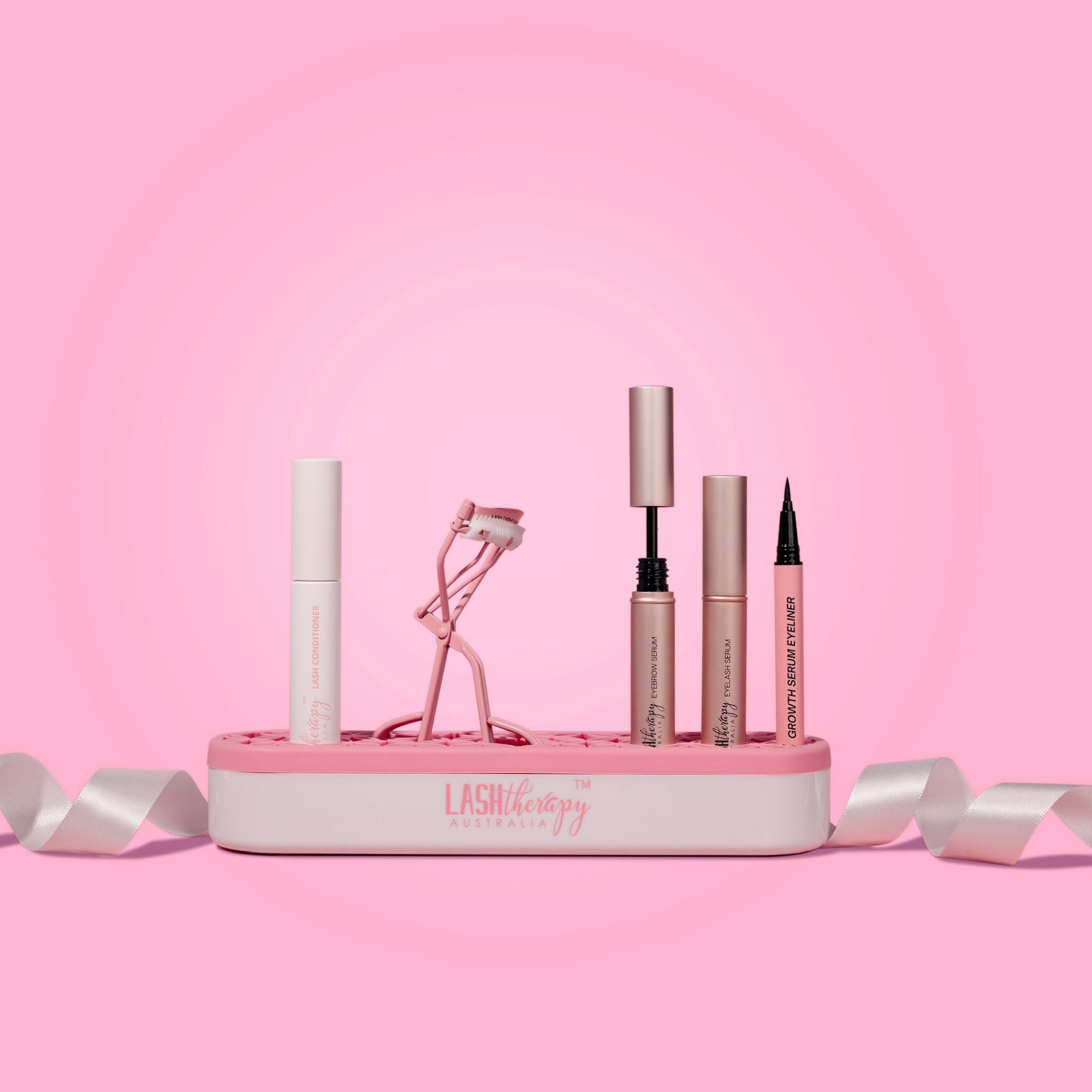 Makeup products on a Lash Therapy Australia Makeup Holder pink stand with a pink background